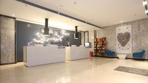 A modern reception area with two reception desks, a large decorative wall art piece, and a seating area with blue chairs. - ECHARM Hotel Zhengzhou High Tech Zone (Zhengzhou)