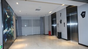 A modern hotel lobby with a large abstract painting, a glass door, and an elevator. - ECHARM Hotel Zhengzhou High Tech Zone (Zhengzhou)