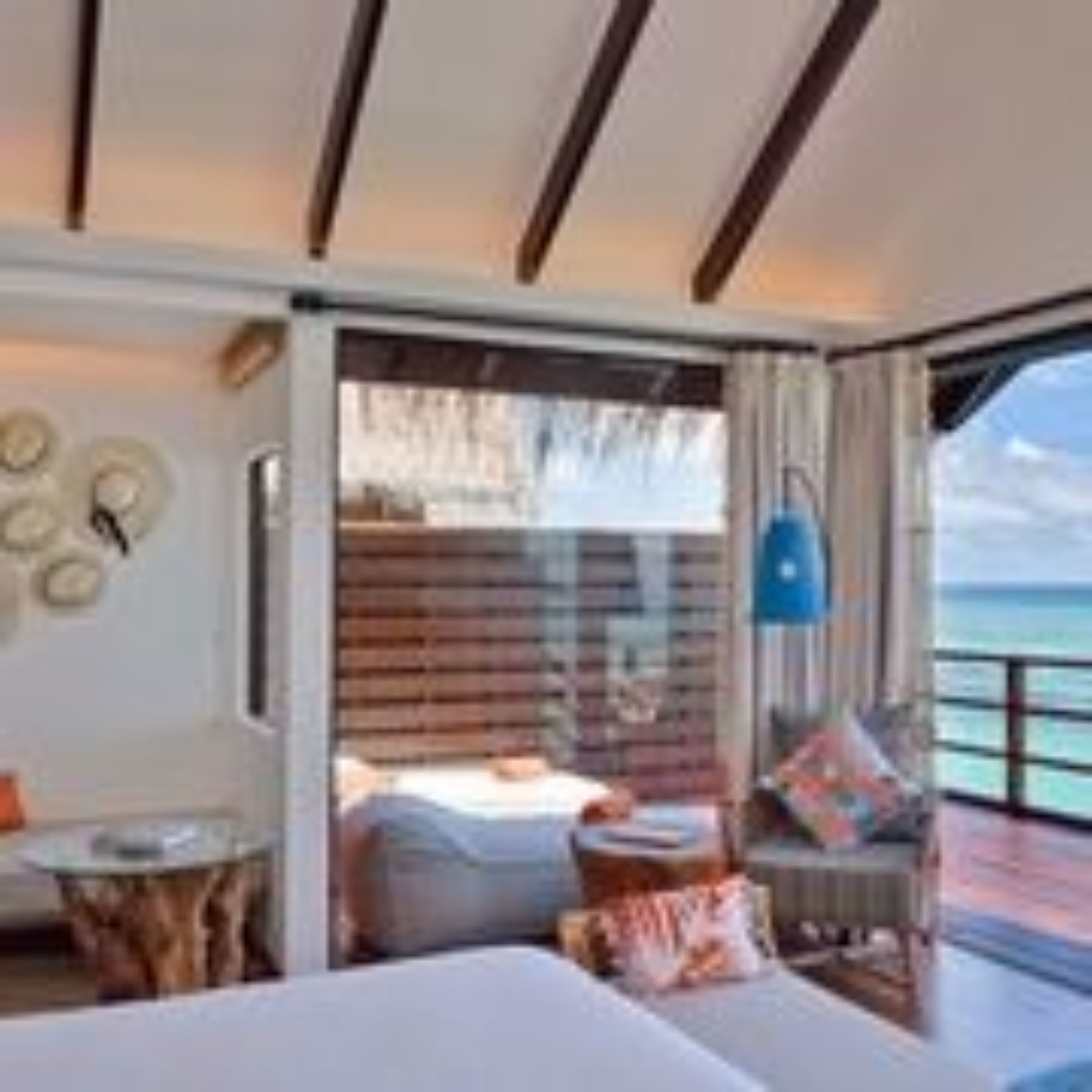 A room with a bed, a small table, a chair, and a view of the sea.