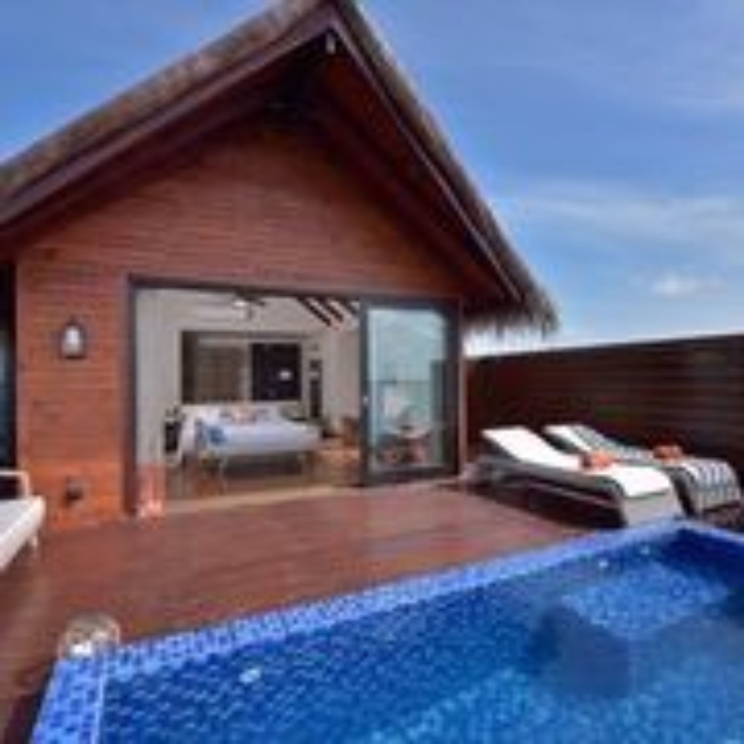 A wooden villa with a pool, a bedroom with a bed and a bathroom, and a dining area.