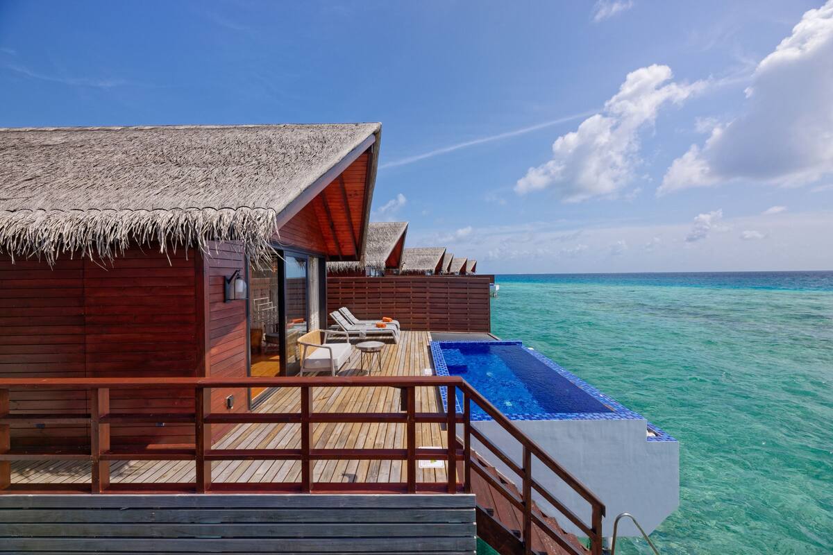 An overwater bungalows with a swimming pool, wooden deck, and thatched roofs.