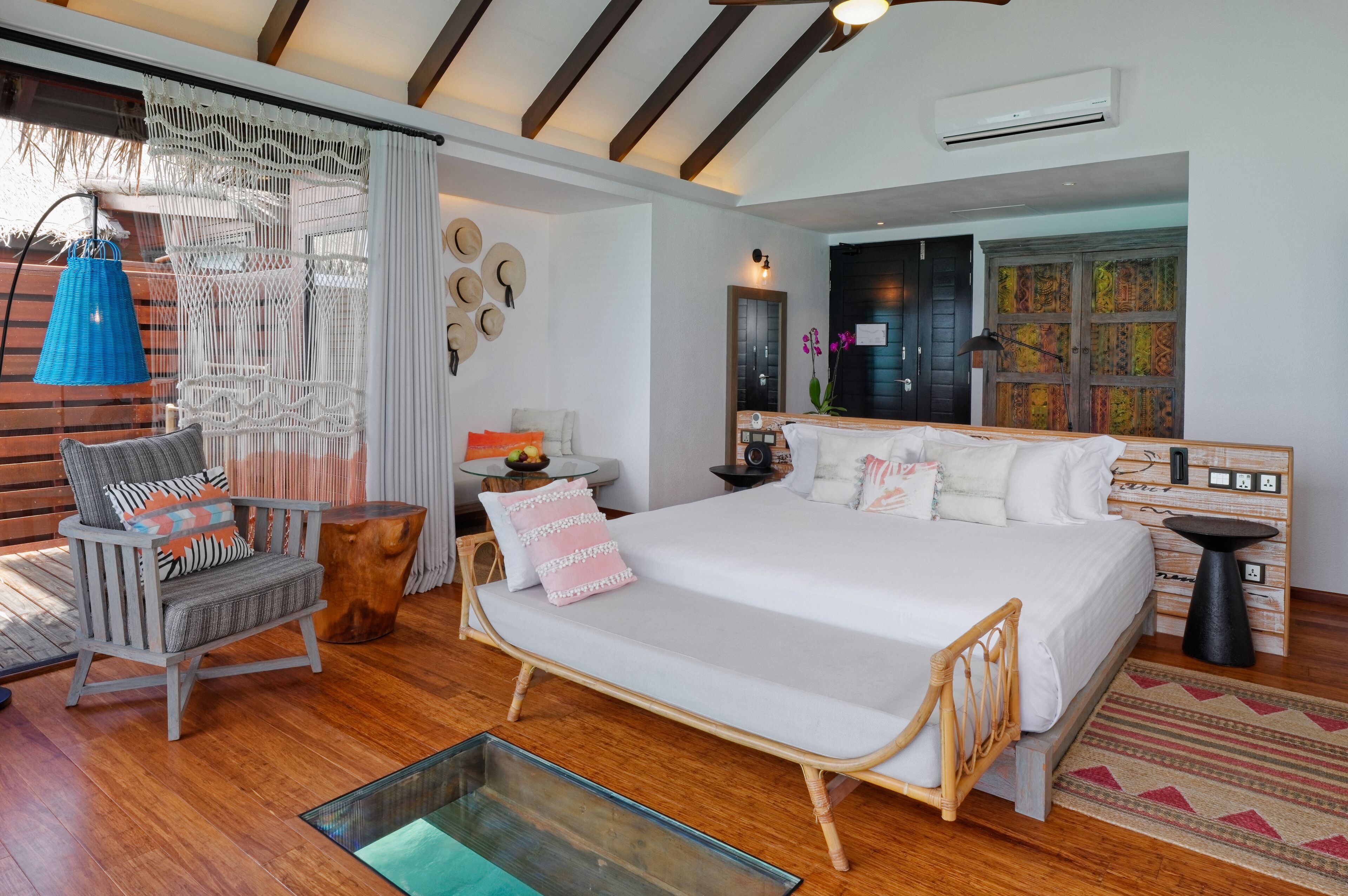 Un dormitorio con una cama grande, una silla de madera, una mesita pequeña y una lámpara colgante.