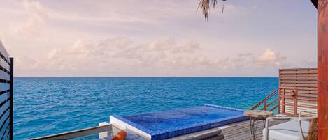 A deck with lounge chairs, a small pool, and a view of the ocean.