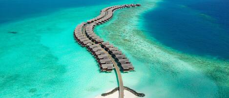 An aerial view of a resort with overwater bungalows connected by a bridge.