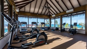 A gym with treadmills, elliptical machines, and exercise balls, overlooking a scenic ocean view.