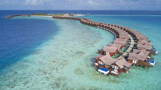 An overwater bungalows with thatched roofs, connected by a walkway, in a clear blue sea. - Grand Park Kodhipparu (Kuda Vattaru)