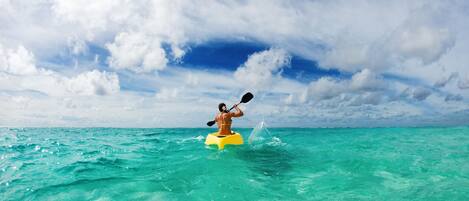 Une personne fait du kayak sur une eau turquoise sous un ciel partiellement nuageux.