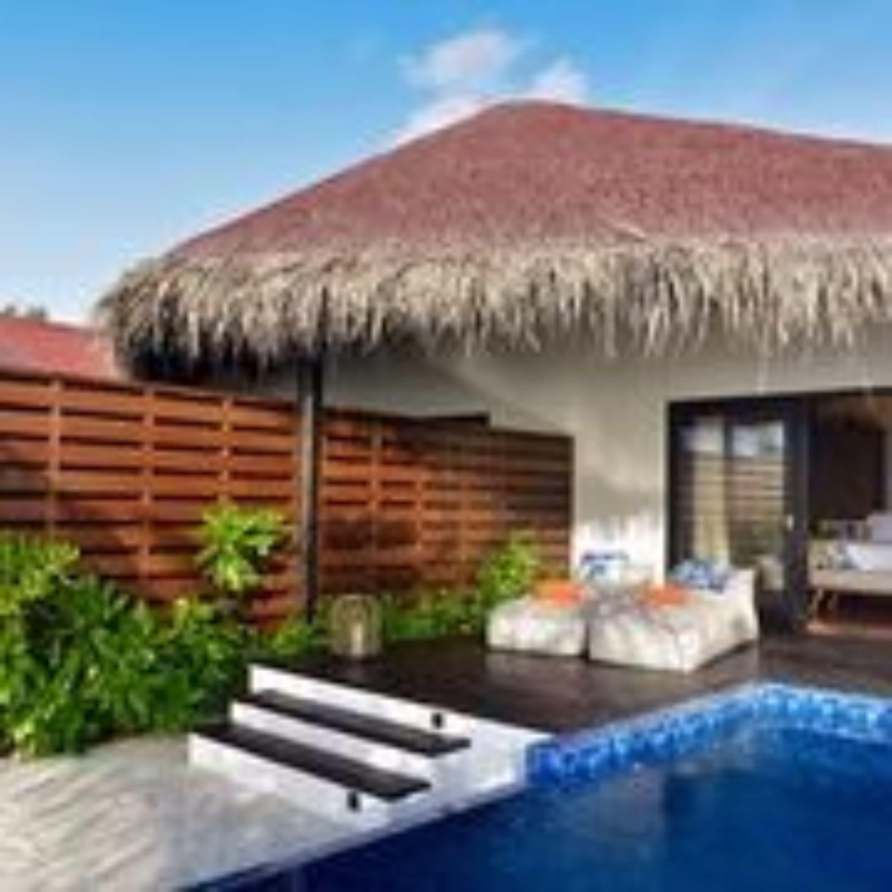 Un resort con piscina, una estructura de techo de paja y una valla de madera.
