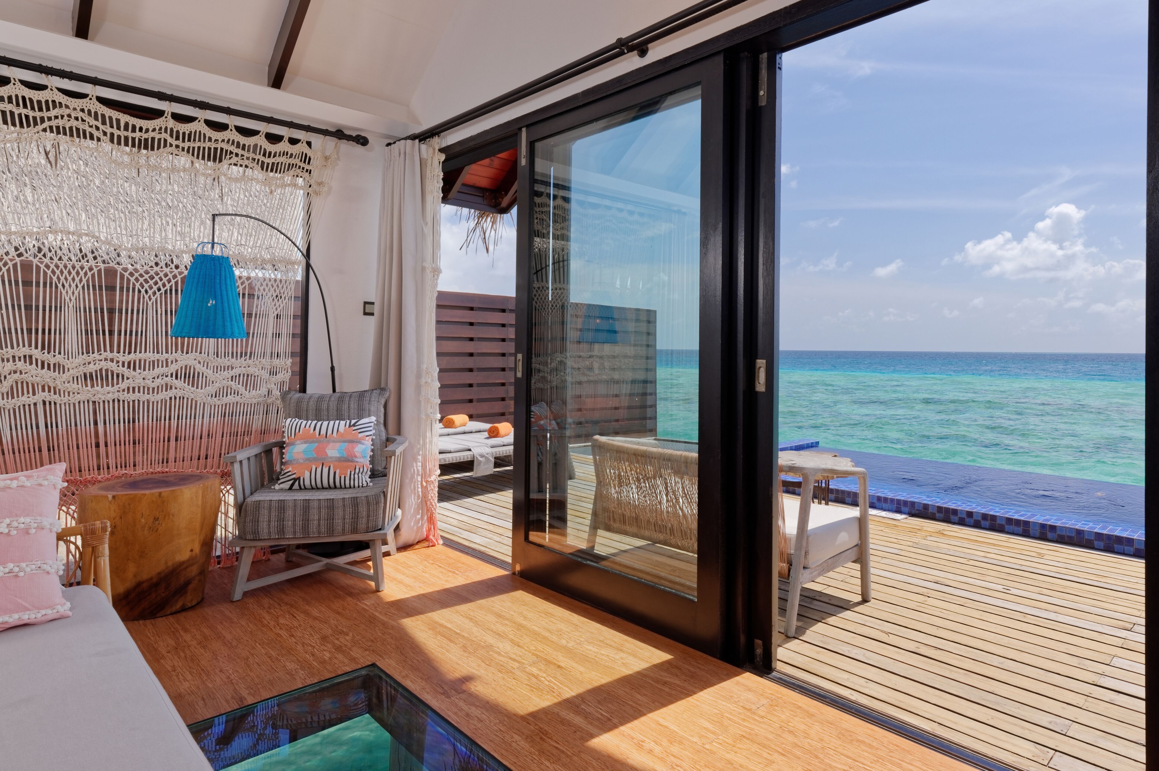 A balcony with a view of the ocean, a wicker chair, a small table, and a sofa with cushions.
