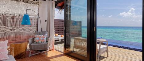 A balcony with a view of the ocean, a wicker chair, a small table, and a sofa with cushions.