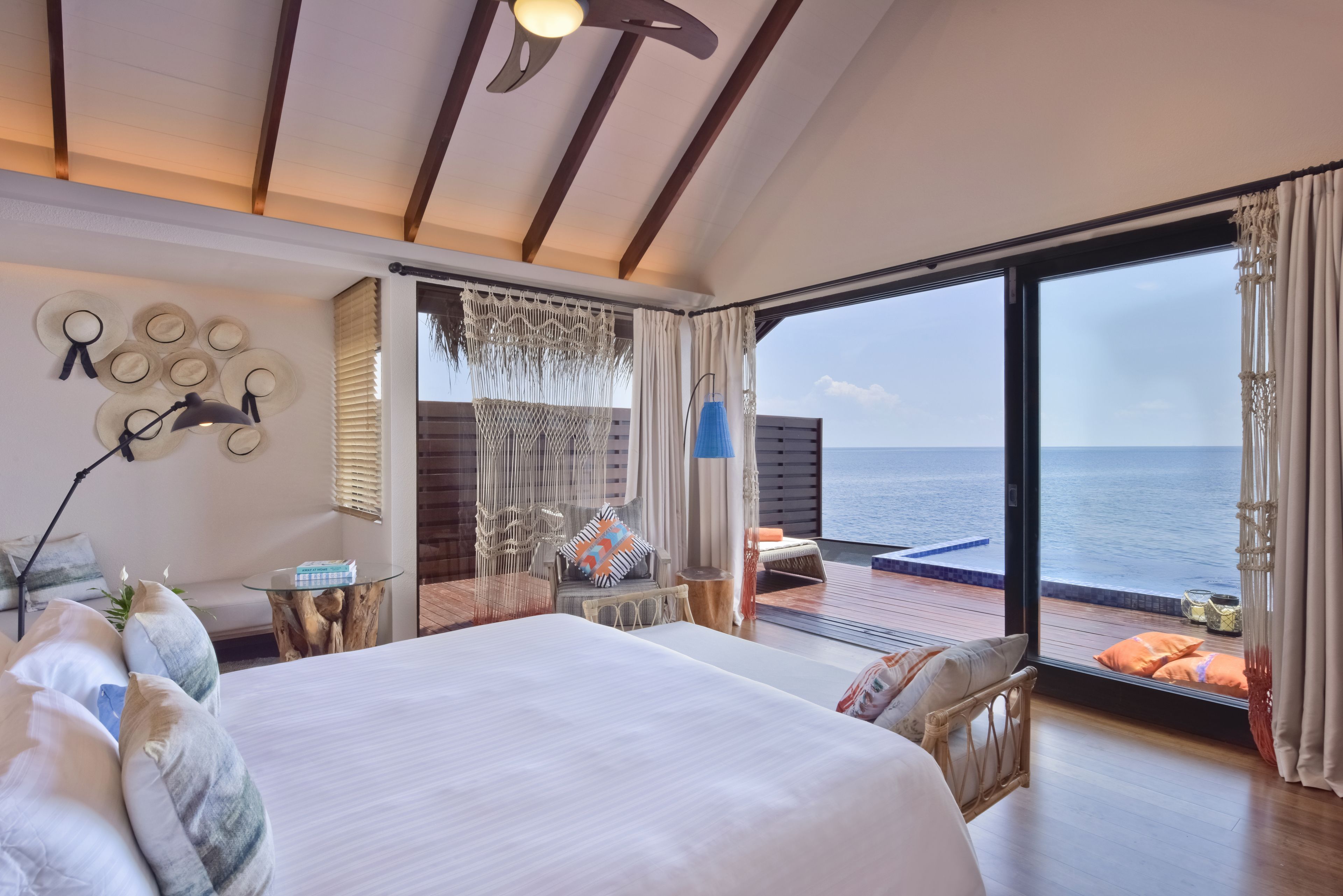 A spacious bedroom with a large bed, a seating area with a view of the sea, and a balcony with a wooden deck.
