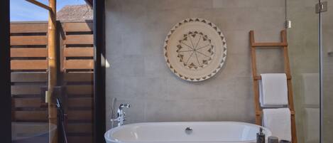 A modern bathroom with a freestanding bathtub, a wooden ladder, and a decorative wall piece.