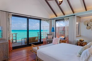 A bedroom with a large bed, a wooden floor, a view of the ocean, a balcony with wicker furniture, and a tropical decor theme. - Grand Park Kodhipparu (Kuda Vattaru)