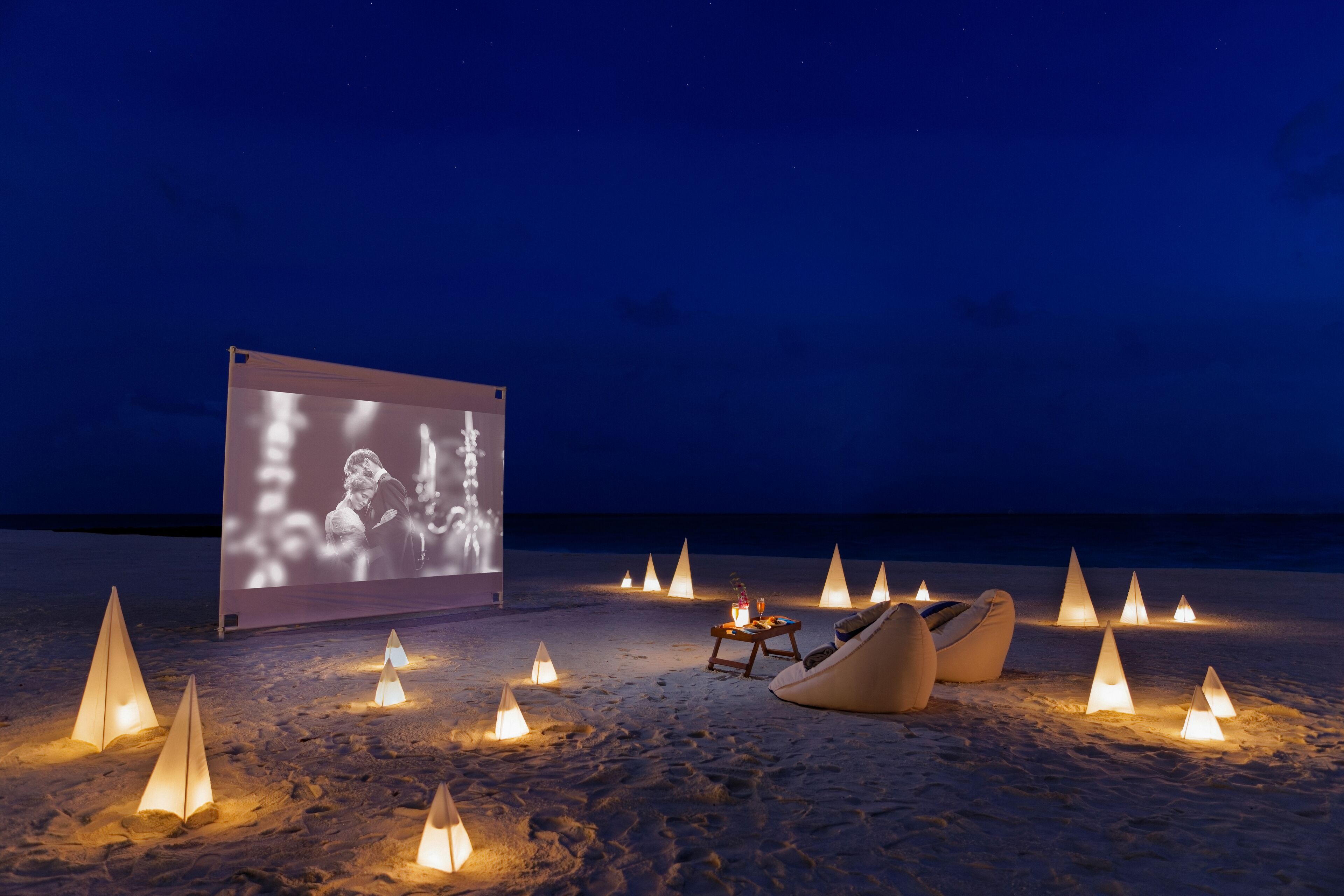 Ein Strandambiente mit einer Projektionsleinwand, Sitzgelegenheiten und beleuchteten Kerzen.