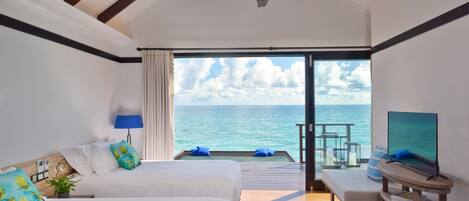 A hotel room with two beds, a TV, a ceiling fan, and a balcony with a view of the sea.