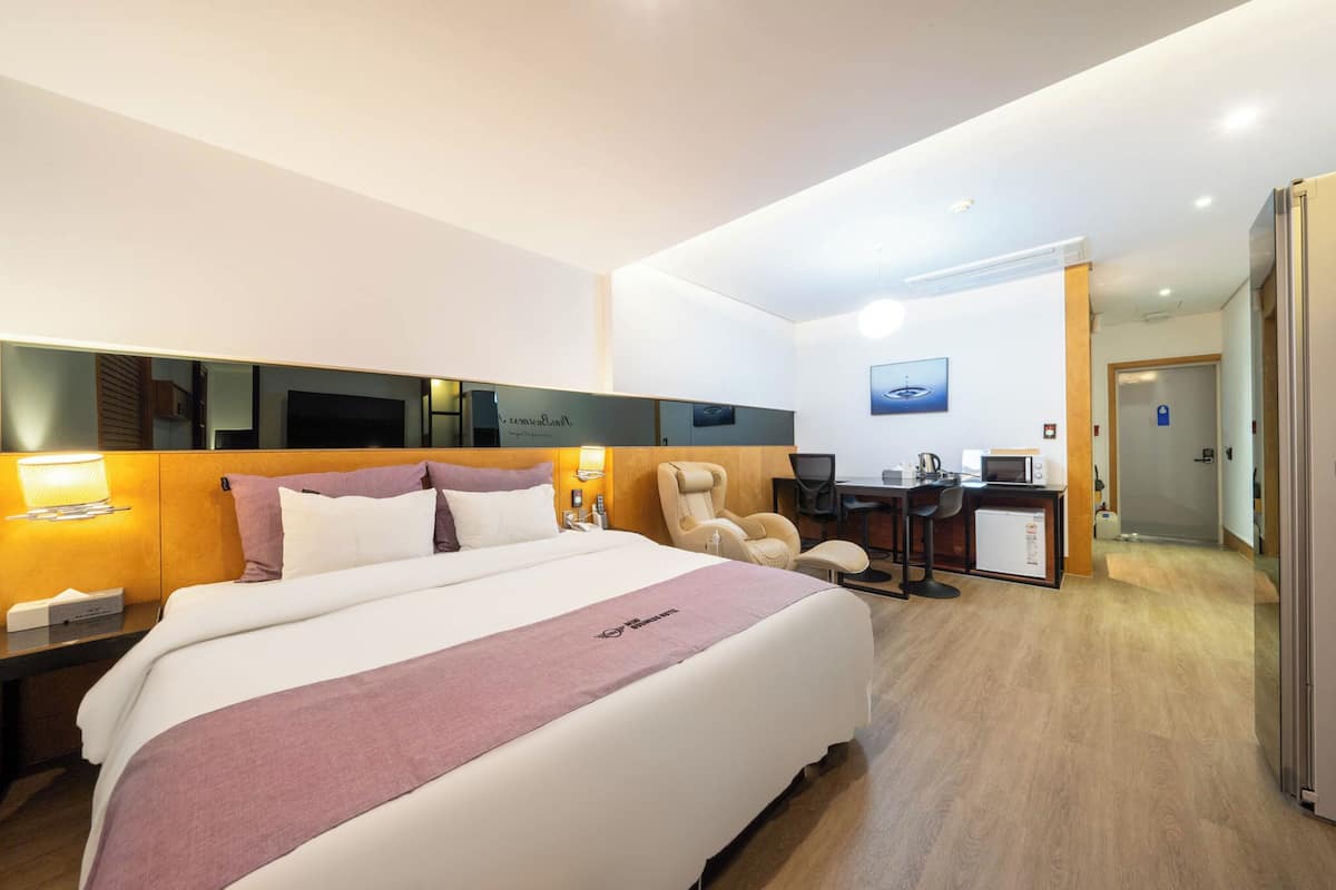 A hotel room with a large bed, a desk with a computer, a chair, and a microwave.
