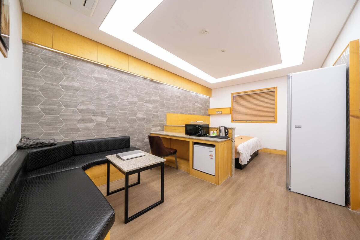 A compact hotel room with a kitchenette, a seating area, and a bed.