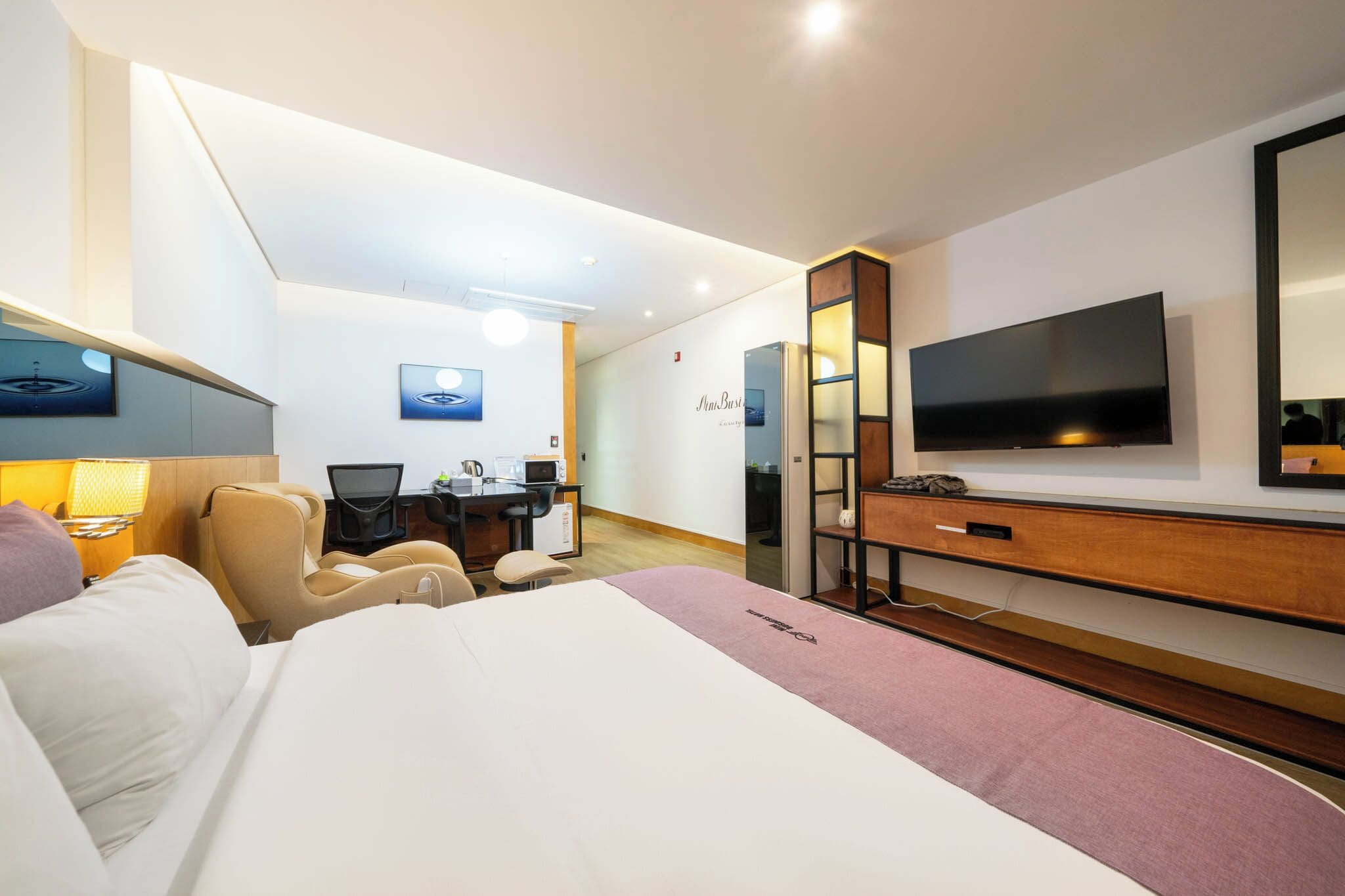 A hotel room with a bed, desk, chair, TV, and a minibar.