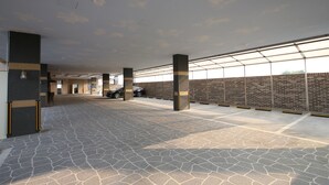 A spacious parking area with a patterned floor, columns, and a brick wall. - JinCheon Mini Business Hotel (Jincheon)