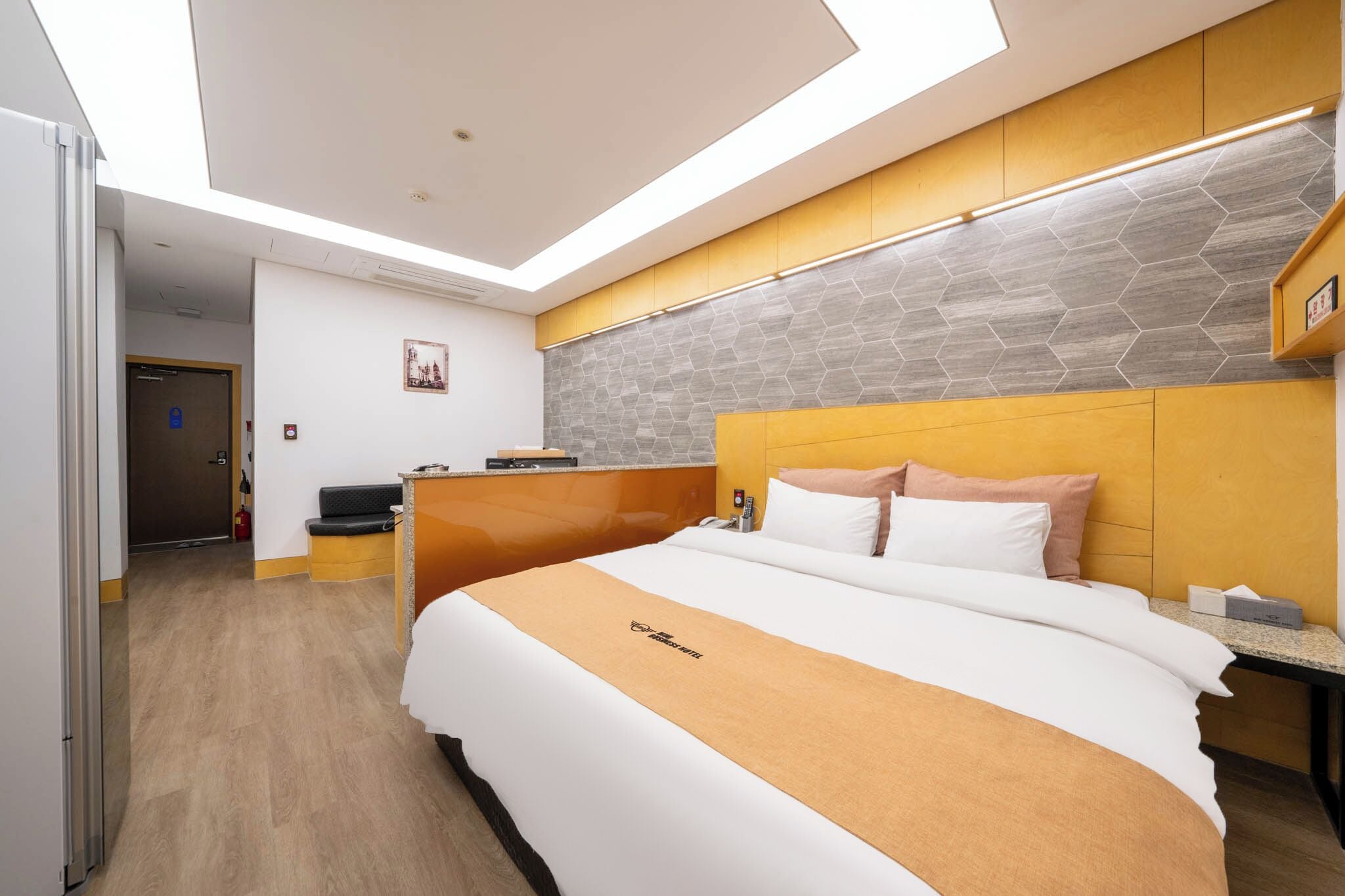 A modern hotel room with a large bed, a wooden headboard, a stone-patterned wall, and a skylight.