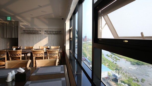 A dining area with wooden chairs and tables, large windows with a view of a river and buildings, and a patterned wall. - JinCheon Mini Business Hotel (Jincheon)