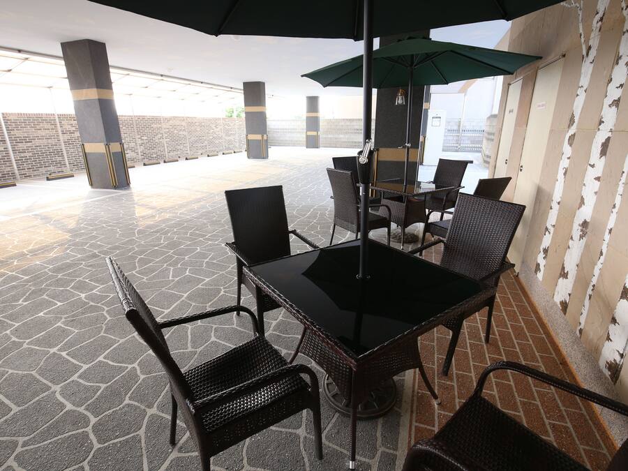 An outdoor patio with a glass table and chairs, surrounded by stone flooring and a brick wall.