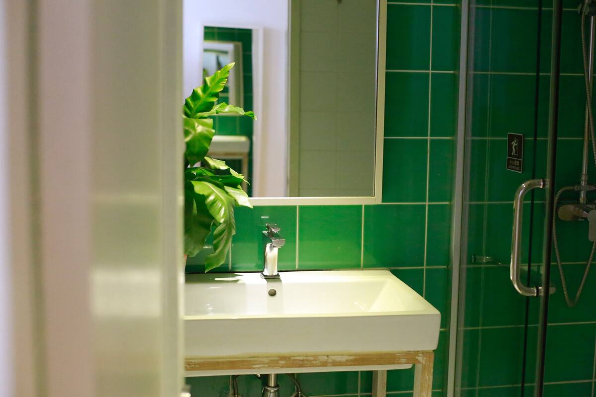 Un baño con un lavamanos blanco, azulejos verdes, un espejo y una zona de ducha.