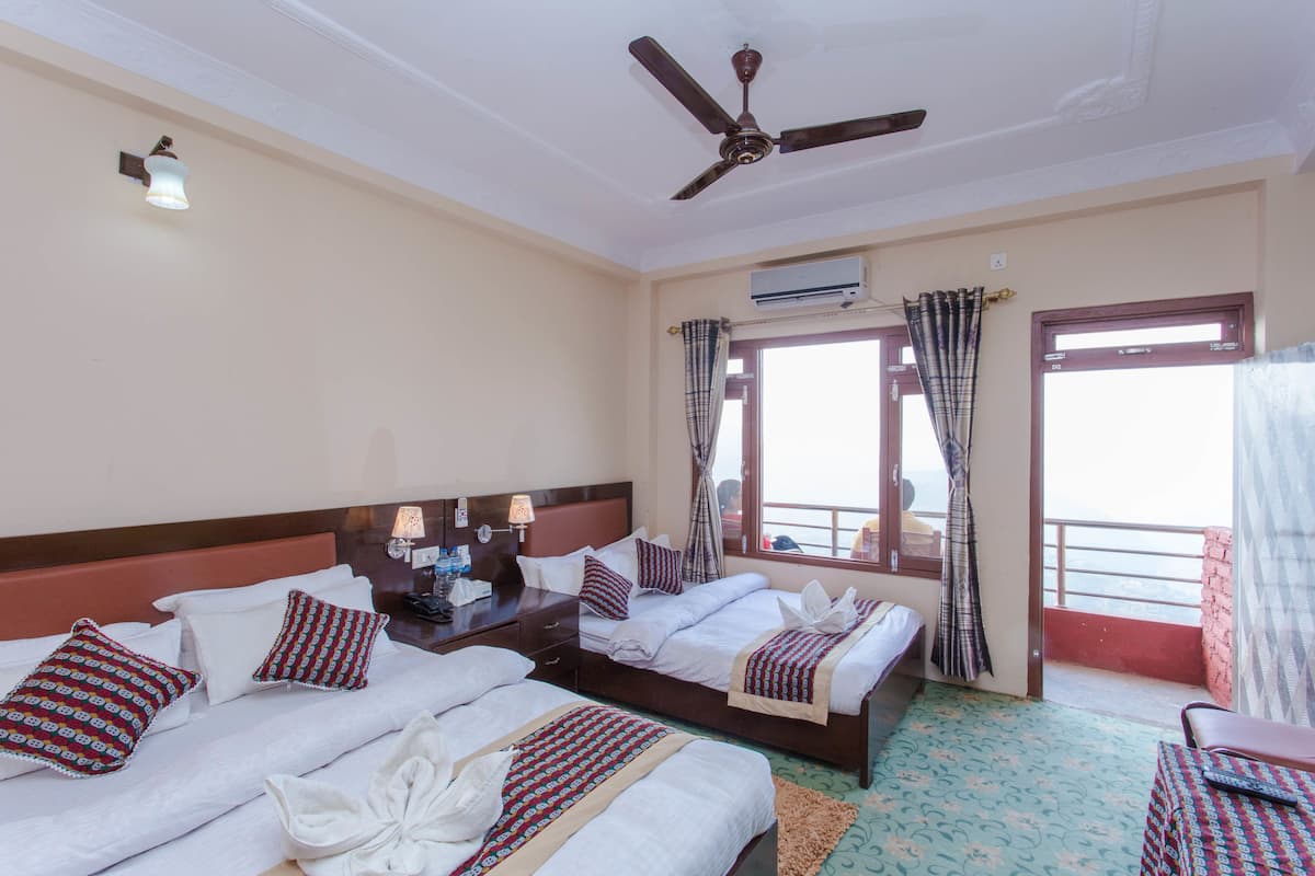 Habitación de hotel con tres camas, ventilador de techo, aire acondicionado y balcón con cortinas.
