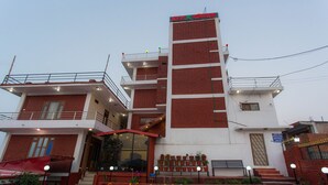 A multi-story building with a red and white facade, a balcony with railings, and a staircase leading to the entrance.