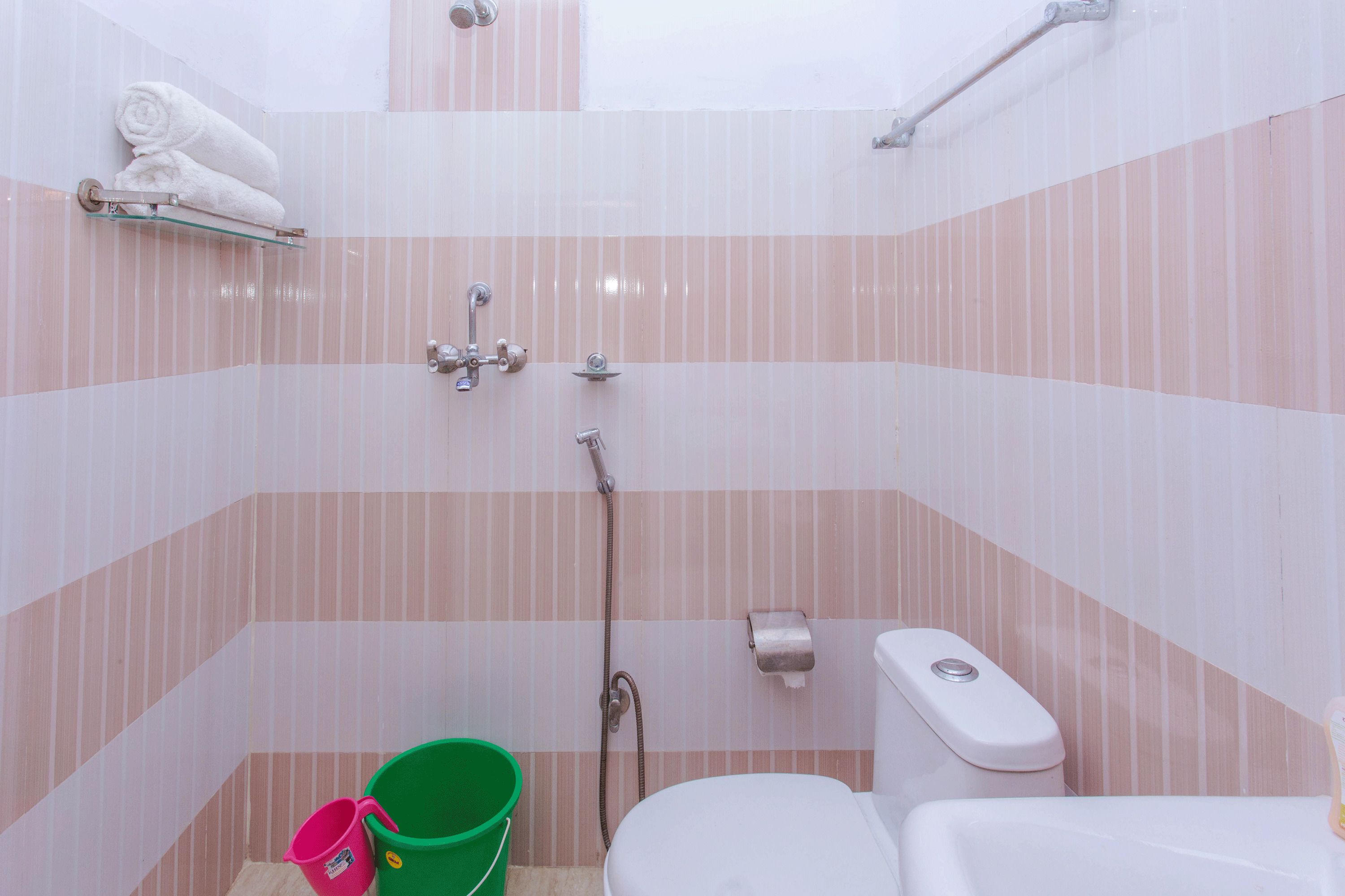 Casa de banho com paredes listradas, um toalete, um chuveiro, um balde verde e um porta-toalhas.