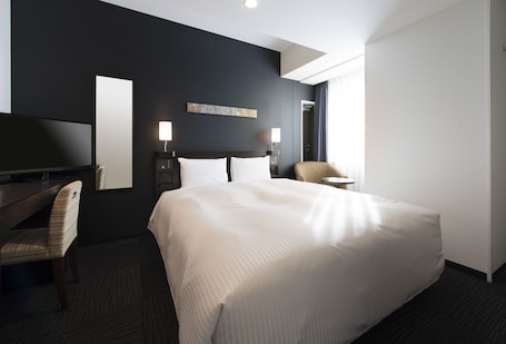 A hotel room with a large bed, a desk with a chair, a TV, two bedside lamps, and a window with curtains.