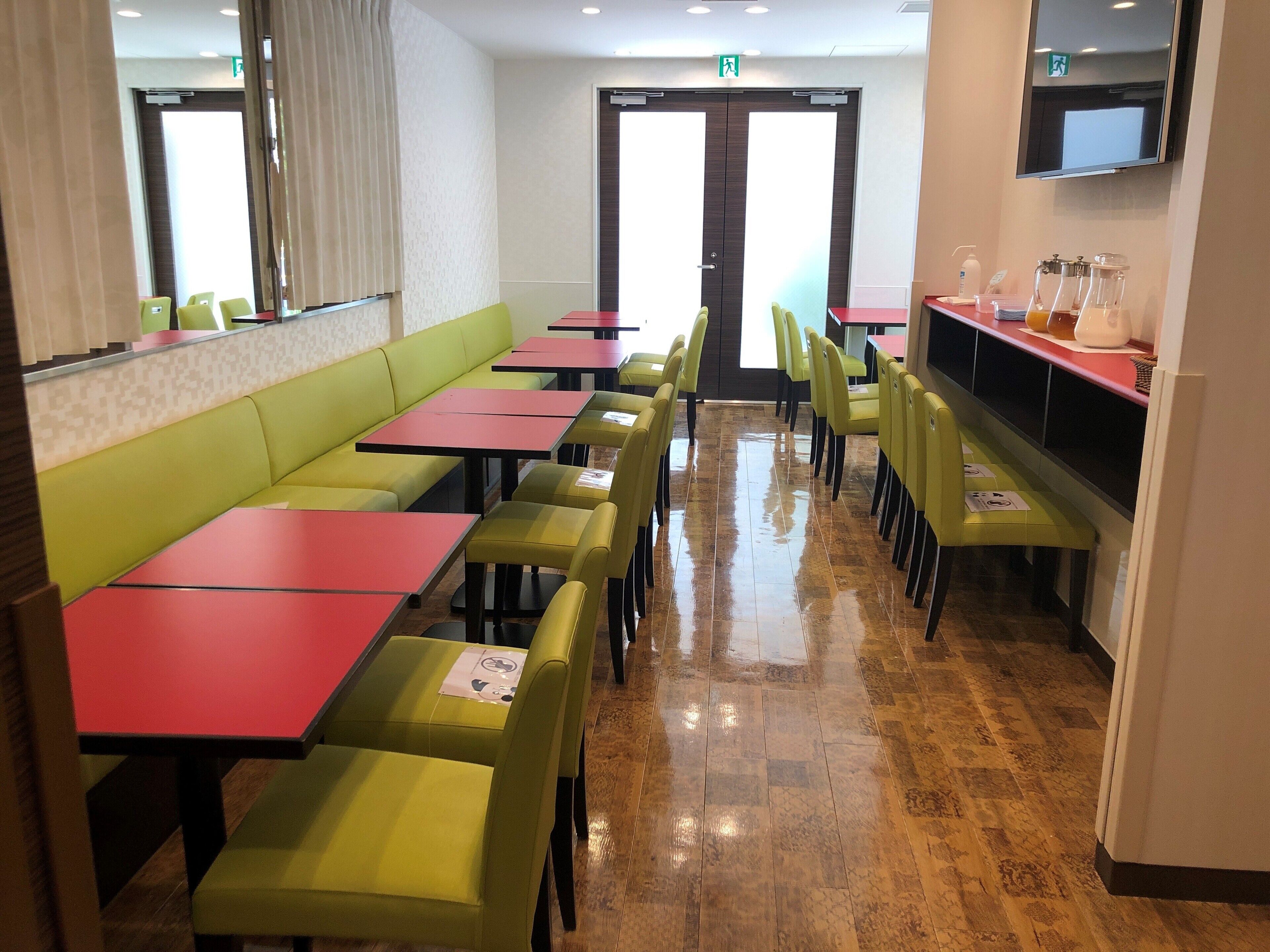 A restaurant with booths and tables, a TV mounted on the wall, and a counter with a beverage dispenser.