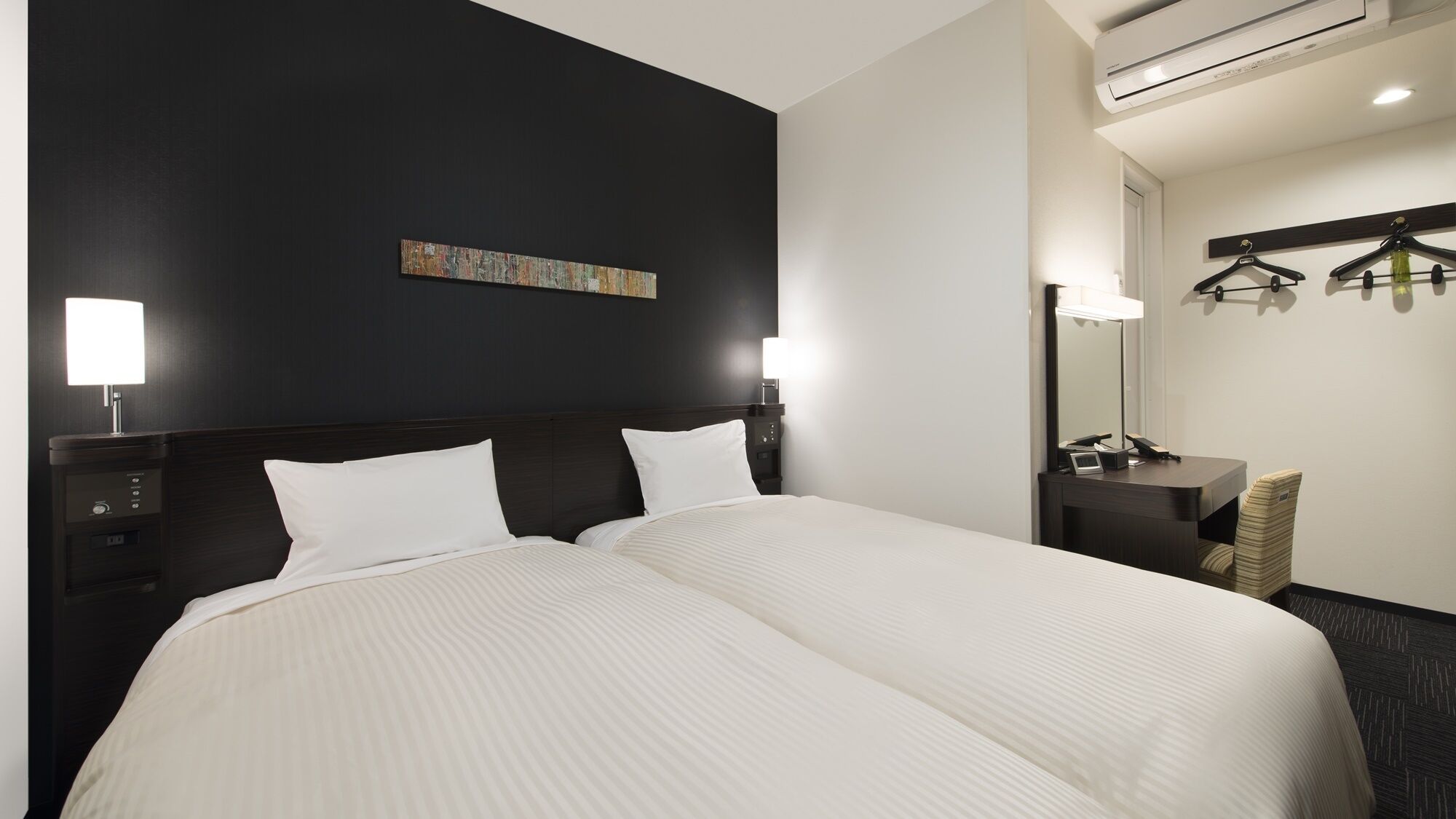 Ett hotellrum med en stor säng, sänglampor, ett nattduksbord, en spegel och en väggmonterad klädhängare.