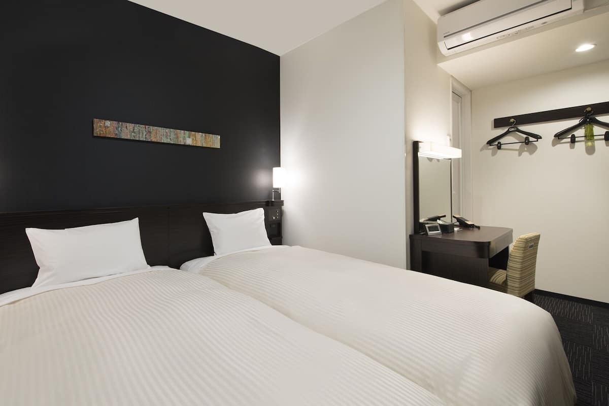 Et hotelværelse med en stor seng, sengeborde, lamper, et spejl og et vægmonteret knagered.