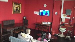 Een woonkamer met rode muren, een aan de muur bevestigde televisie, een klok, een open haard en een eethoek met stoelen en een tafel.