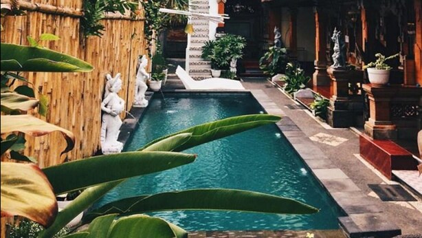 A pool area with a bamboo fence, statues, and potted plants. - Nyoman Badri Homestay (Ubud)