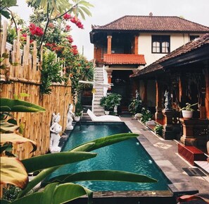 A pool area with a bamboo fence, statues, and potted plants. - Nyoman Badri Homestay (Ubud)
