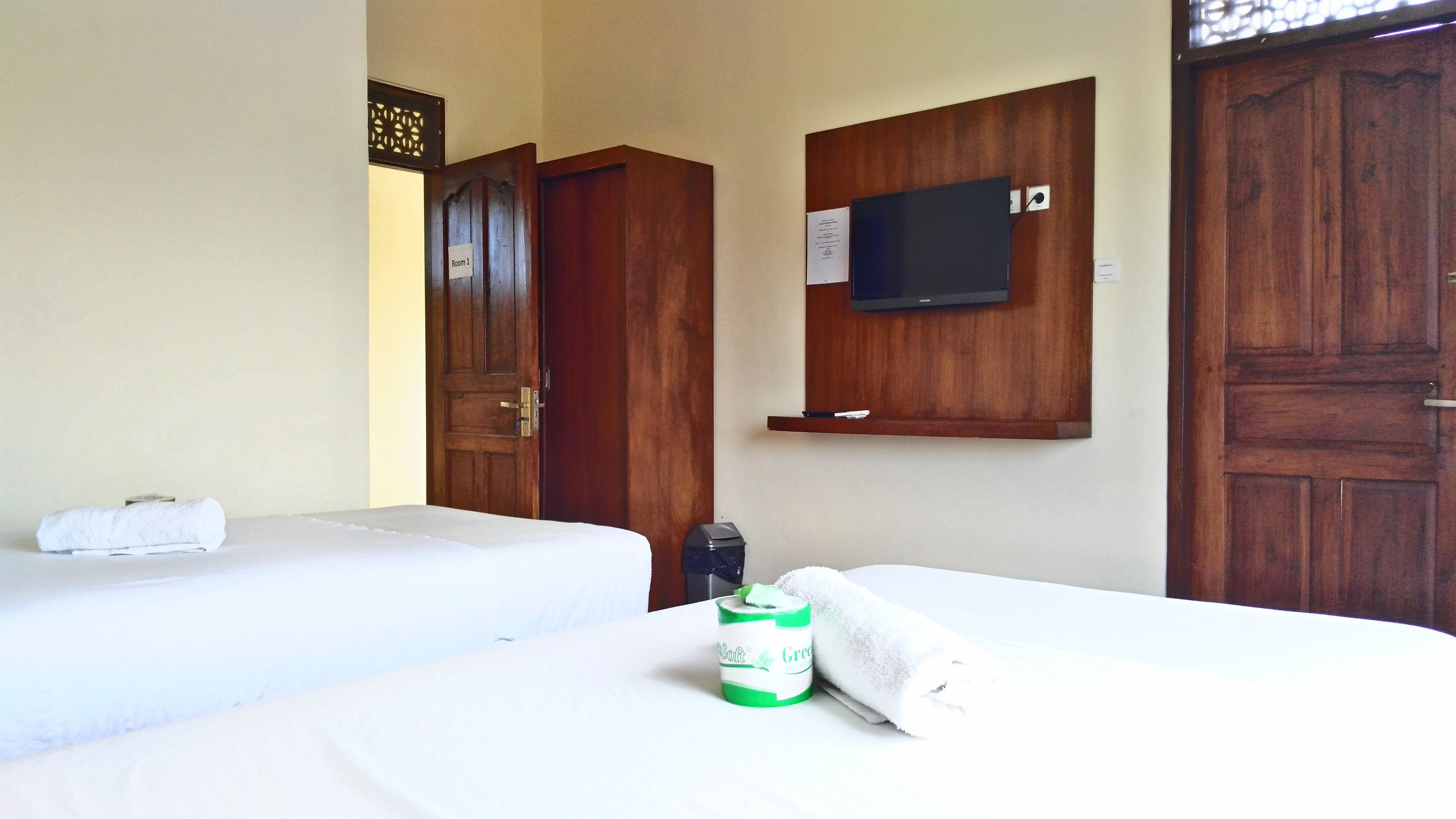A hotel room with two beds, a television mounted on the wall, and a wooden door.
