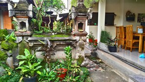A traditional courtyard with stone structures, potted plants, and a dining area with wooden furniture. - Nyoman Badri Homestay (Ubud)