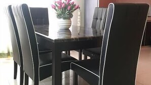 Un coin repas avec une table et des chaises noires, un vase de fleurs et, au fond, une cuisine.