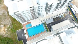 Vue aérienne d’un bâtiment moderne doté d’une piscine sur le toit, de nombreux balcons et d’un espace de stationnement.