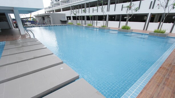 Une piscine avec des marches carrelées et une terrasse en bois, entourée d’un bâtiment moderne doté de balcons.