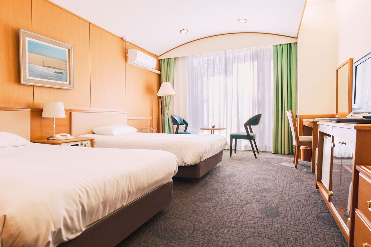 A hotel room with two beds, a desk, a chair, a TV, and a window with curtains.