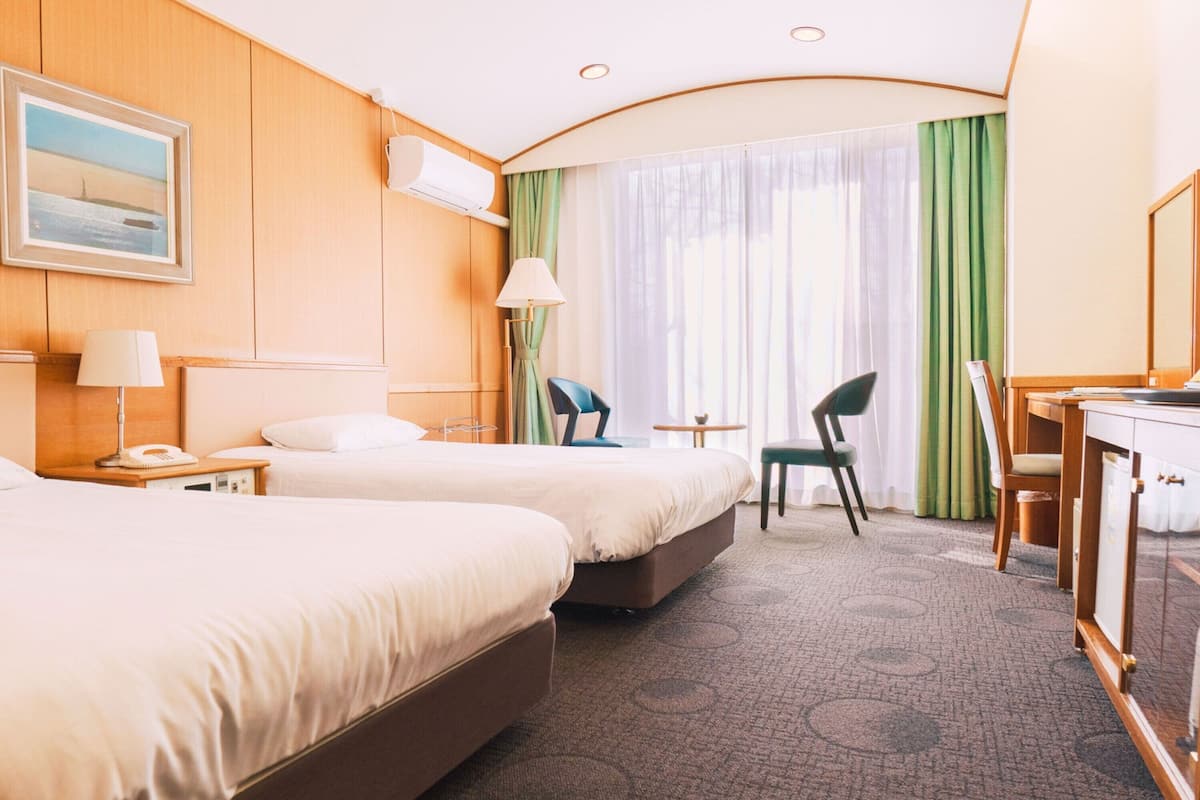 A hotel room with two beds, a desk, a chair, a lamp, a phone, and a painting on the wall.
