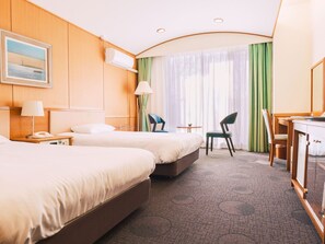 Habitación de hotel con dos camas, un escritorio, una silla, una lámpara, un teléfono y un cuadro en la pared.