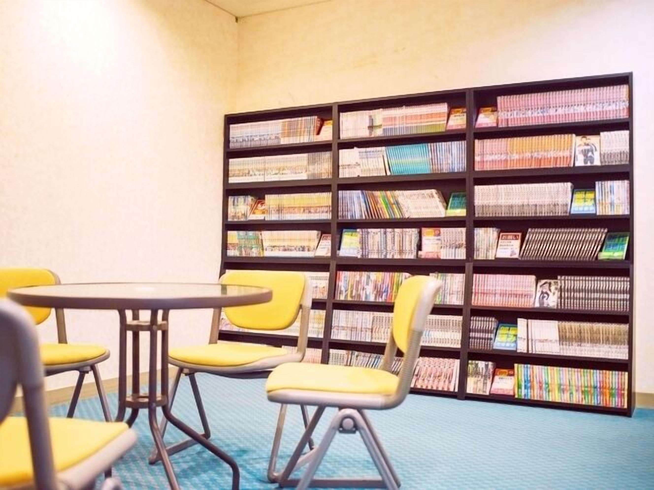 A room with a bookshelf filled with books, a round table, and four yellow chairs.