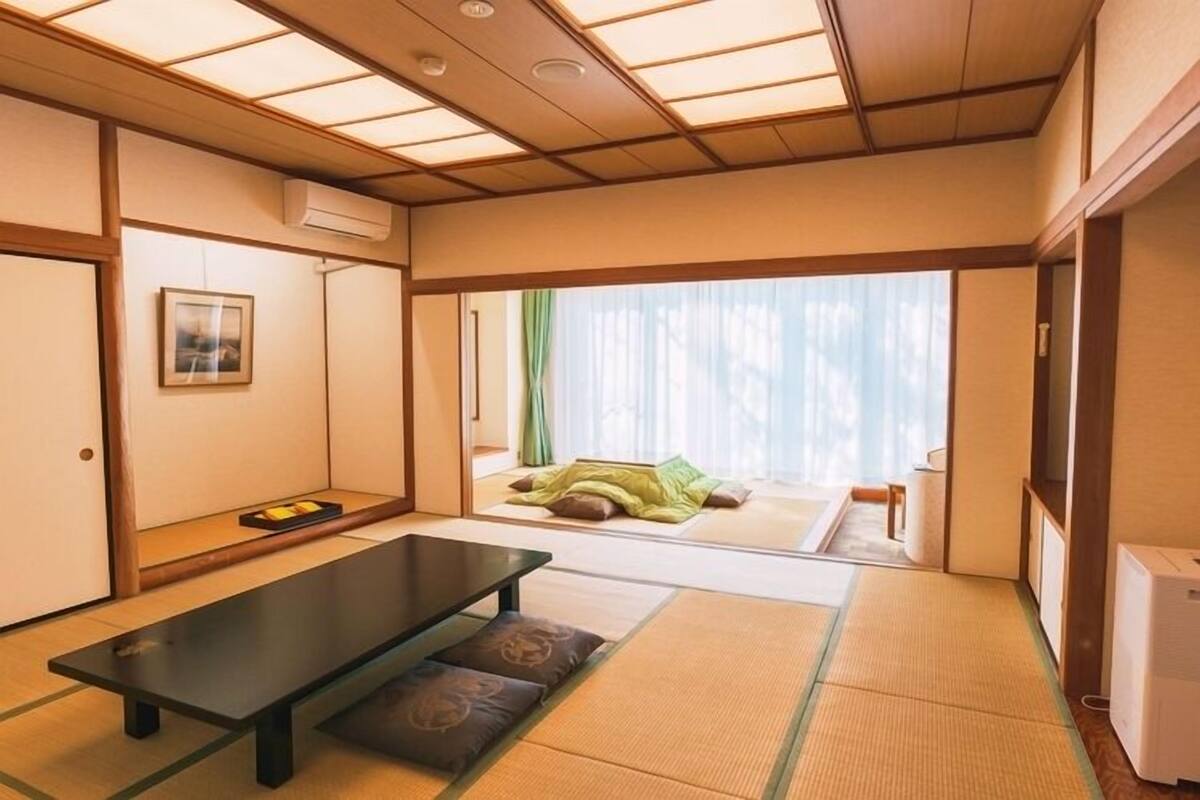 A traditional Japanese room with tatami flooring, a low table, and sliding doors leading to a balcony.