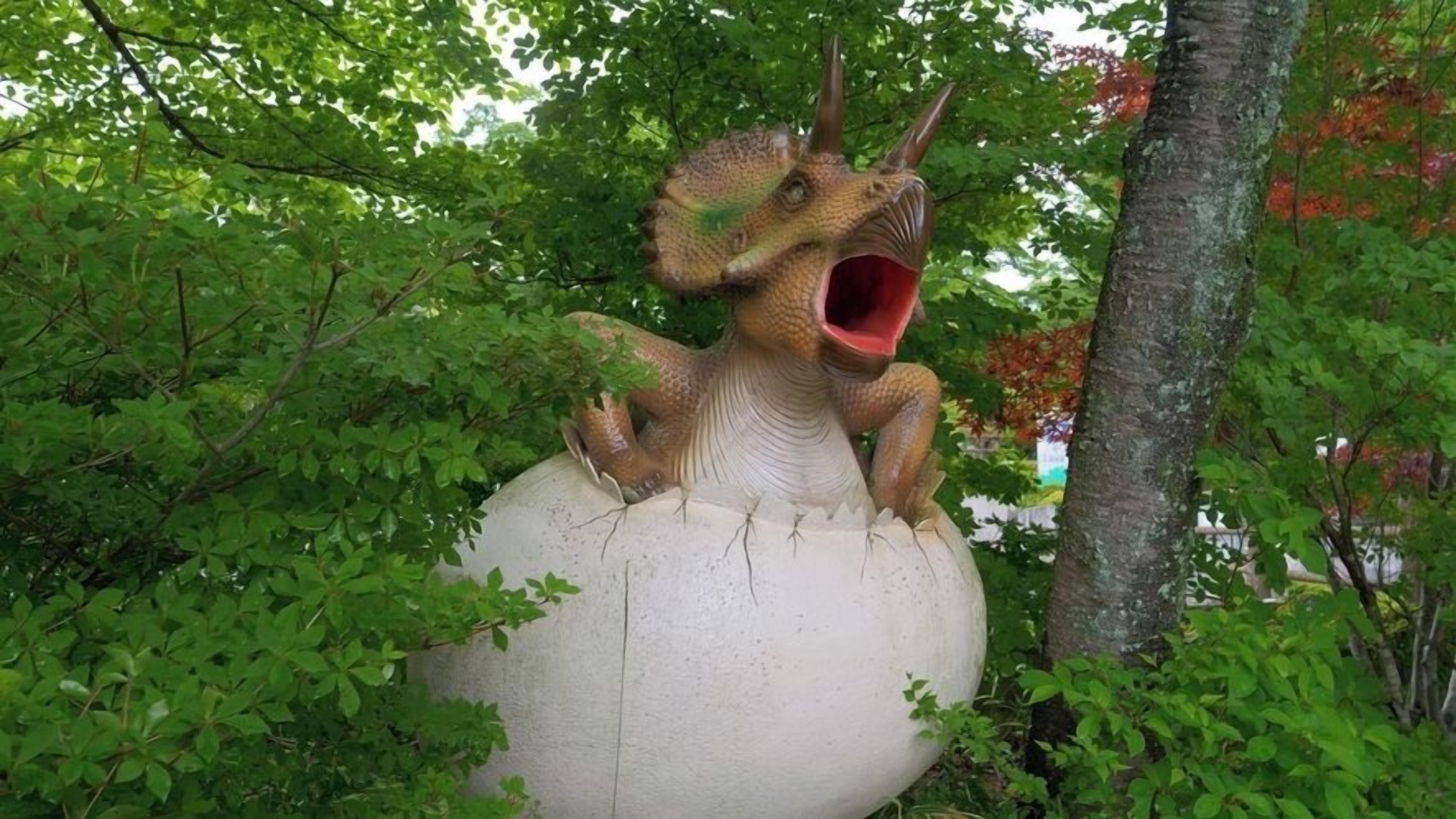Una gran escultura de dinosaurio con la boca muy abierta, rodeada de frondosa vegetación.
