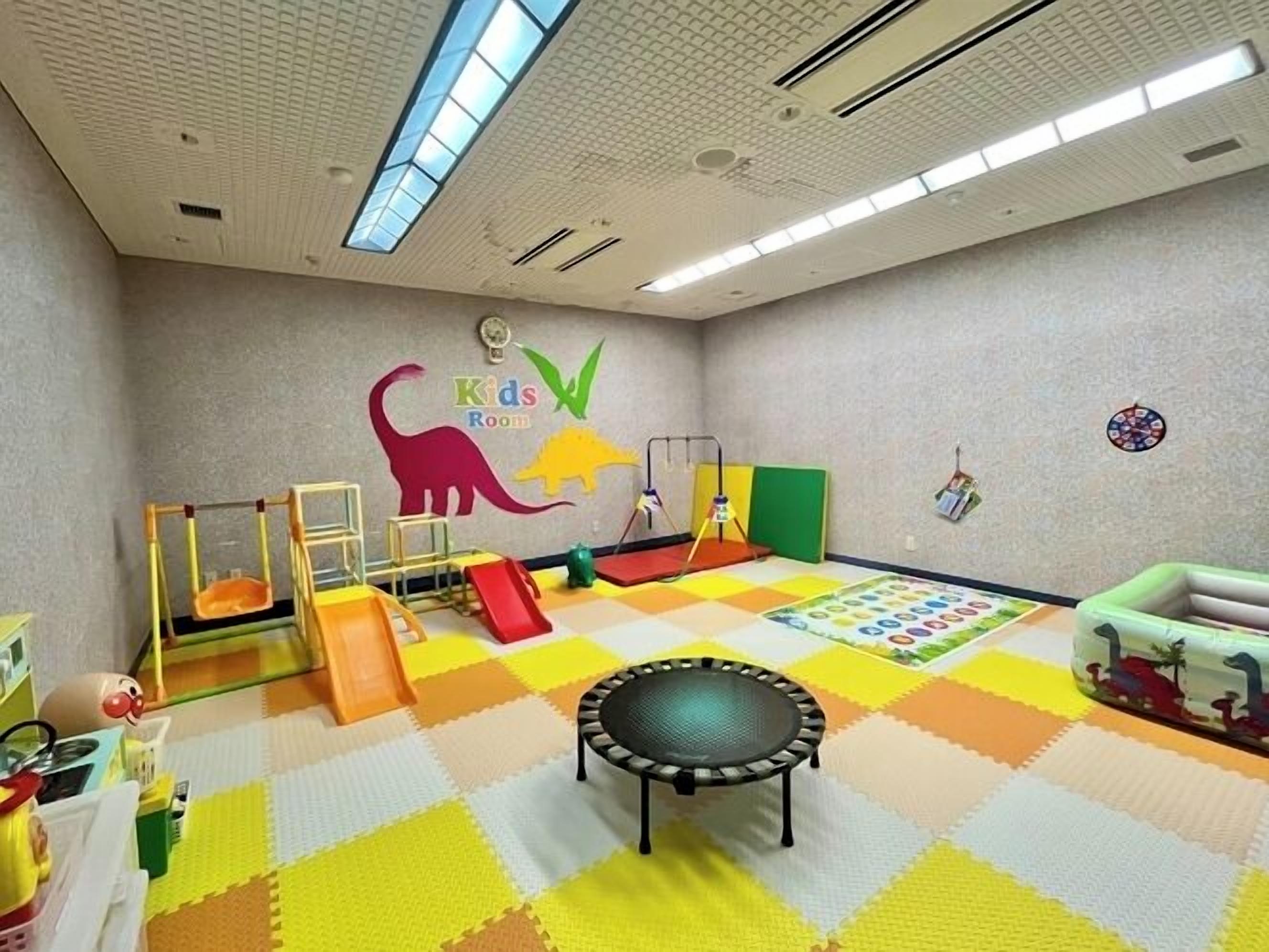 A children's playroom with a colorful floor, play structures, and a wall-mounted dinosaur mural.