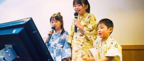 A group of children performing on stage with musical instruments and a microphone stand.